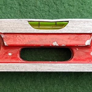 Puede incluir: Un nivel de burbuja rojo y plateado con dos viales de burbuja y un indicador de nivel de líquido verde.