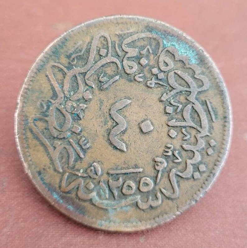 May include: A copper coin with Arabic script around the edge and a large number "2" in the centre. The coin is slightly worn and has a greenish patina.