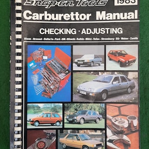 May include: A Snap-on Tools Carburettor Manual from 1983. The cover features a variety of tools and cars, including a red toolbox, a silver car, and a white car. The manual is for checking and adjusting carburettors for various brands, including Aisan, Bressel, Dellorto, Ford, GM, Hitachi, Keihin, Nikki, Solex, Stromberg, SU, Weber, and Zenith.