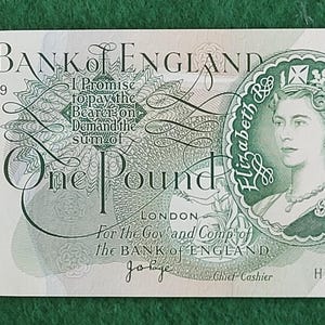 May include: A Bank of England one-pound note, predominantly green and white. It displays a portrait of Queen Elizabeth II and the text "One Pound". The note also features the text "Bank of England" and the serial number HZ56 801119.