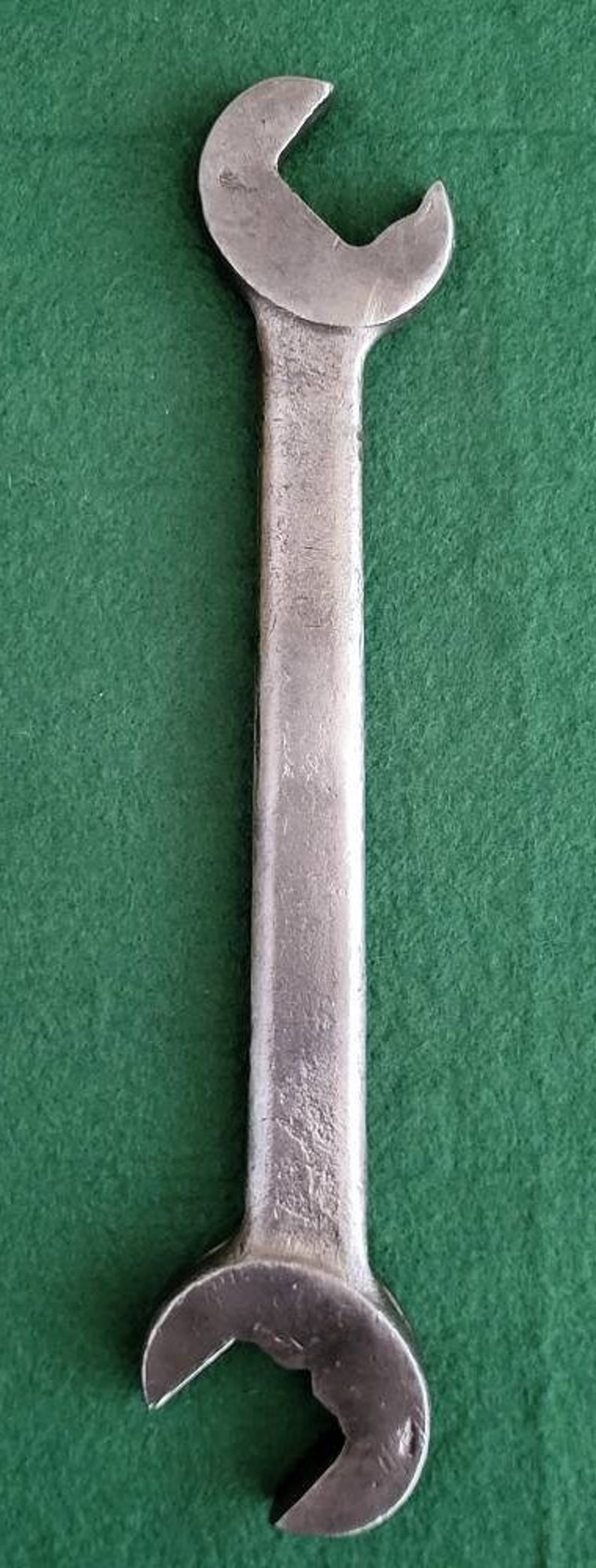 K&ouml;nnte beinhalten: Ein silberner Schraubenschl&uuml;ssel mit einem geschlossenen Ende und einem offenen Ende. Der Schraubenschl&uuml;ssel liegt auf einer gr&uuml;nen Oberfl&auml;che.