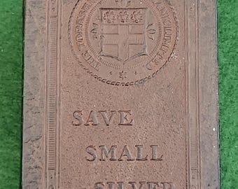 May include: A brown antique book cover with gold corner protectors. The cover has embossed text reading "SAVE SMALL SILVER" and a circular emblem with text and a crest. The book is set against a green background.