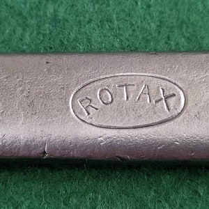 K&ouml;nnte beinhalten: Nahaufnahme eines silbernen Metallobjekts mit dem Wort "ROTAX" in einer ovalen Form gepr&auml;gt.