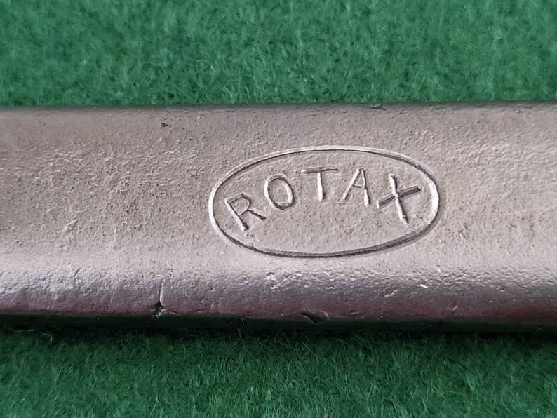 K&ouml;nnte beinhalten: Nahaufnahme eines silbernen Metallobjekts mit dem Wort "ROTAX" in einer ovalen Form gepr&auml;gt.