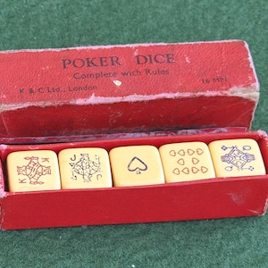 May include: A red box, marked "POKER DICE" and "Complete with Rules", holds five ivory dice. Each die features playing card symbols. The box also has the text "K & C Ltd., London" and "16 MM". The dice are inside a red box.