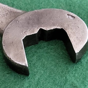 K&ouml;nnte beinhalten: Nahaufnahme eines silbernen Schraubenschl&uuml;ssels mit abgerundetem Kopf und einer einzigen Markierung oben. Der Schraubenschl&uuml;ssel liegt auf einer gr&uuml;nen Oberfl&auml;che.