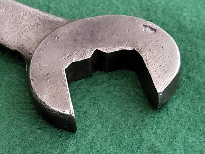 K&ouml;nnte beinhalten: Nahaufnahme eines silbernen Schraubenschl&uuml;ssels mit abgerundetem Kopf und einer einzigen Markierung oben. Der Schraubenschl&uuml;ssel liegt auf einer gr&uuml;nen Oberfl&auml;che.