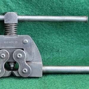 Puede incluir: Una herramienta de cadena de bicicleta de metal plateado con un mango de resorte y la palabra "REYNOLDS" impresa en el lateral.