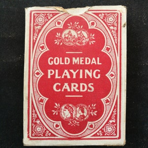 以下が含まれることがあります： 赤と白を基調とした、ヴィンテージのトランプの箱。 白い文字で「GOLD MEDAL PLAYING CARDS」と書かれています。 デザインには、花柄やメダリオンのモチーフが含まれており、クラシックなスタイルを連想させます。