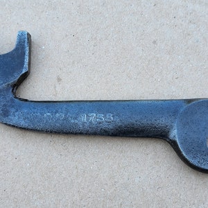Op de afbeelding: Een zwarte metalen sleutel met een unieke gebogen handgreep en een markering 1755. De sleutel heeft aan het ene uiteinde een standaard open-eind sleutelkop en aan het andere uiteinde een gespecialiseerde kop.