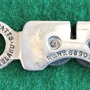 Peut inclure: Un aiguiseur de couteaux argenté avec une poignée circulaire et une section d'affûtage rectangulaire. La poignée porte l'inscription "SHEFFIELD ENGLAND JOHN WATTS". La section d'affûtage porte l'inscription "REG.NO.639039."