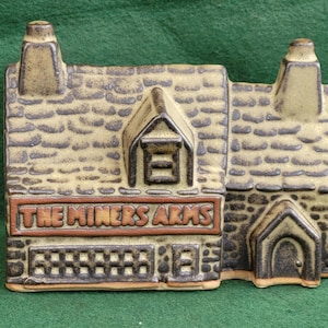 Könnte beinhalten: Ein Keramikmodell eines Pubs mit einer braunen und beigefarbenen Backsteinfassade. Das Schild lautet "The Miners Arms".