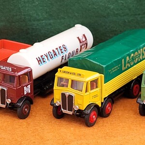 May include: A collection of vintage toy trucks in various colors, including red, maroon, yellow, and green. Each truck features detailed designs and branding, with some carrying cargo. The trucks are arranged on an orange surface.