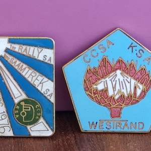 May include: Four metal enamel pins. The first is a blue circle with '1977 RALLY S.A. SAAMTREK' and a diamond graphic. The second is a blue rectangle with 'RALLY SA SAAMTREK SA SPRINGS 1976'. The third is a light blue pentagon with 'CCSA K.S.A WESIRAND'. The fourth is an oval with a bird, 'CCSA-K.S.A' and 'NORTH RAND'.