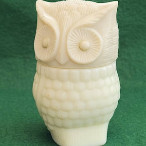May include: A white ceramic owl-shaped bottle with a textured surface. The owl has large, round eyes and a detailed beak.
