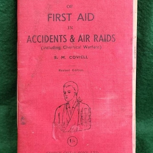 Puede incluir: Un libro rojo titulado "The Pocket Book of First Aid in Accidents & Air Raids (including Chemical Warfare)" de E.M. Cowell. El libro es una edición revisada y cuesta 1/-. Está publicado por George Gill & Sons, Ltd. en Londres.