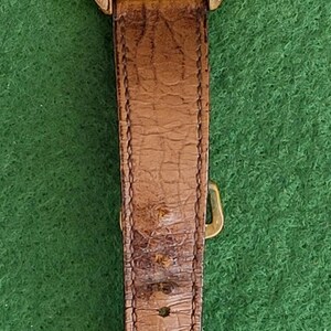 May include: A vintage gold-toned ORIS wristwatch with a light-colored face and a date display at the 3 o'clock position. The watch has gold hands and markers, and a brown leather band. The watch face is approximately 1.25 inches in diameter.