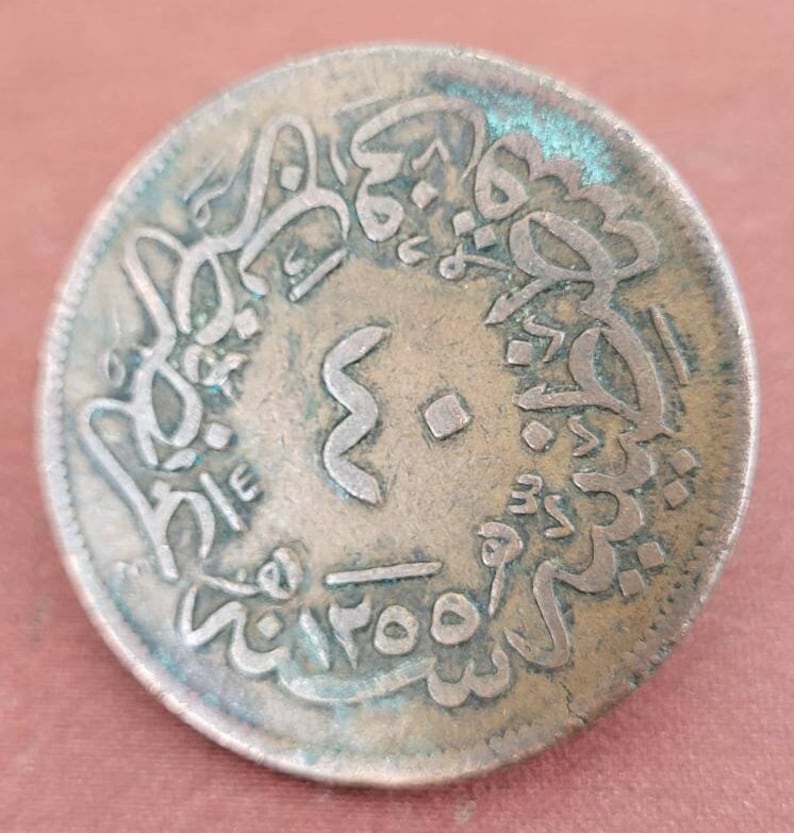 May include: A copper coin with Arabic script around the edge and a symbol in the centre. The coin is slightly tarnished and has a greenish patina.