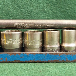 Puede incluir: Un juego de seis vasos de cromo-vanadio en un soporte de metal azul. Los vasos están etiquetados con "ELORA" y están dispuestos en una fila. El soporte tiene una franja pintada de azul en la parte delantera.