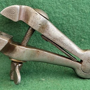 May include: A silver metal clamp with a screw adjustment and a handle. The clamp is marked with the number "2" and the word "Improved".