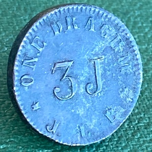 Könnte beinhalten: Eine Nahaufnahme eines silberfarbenen Metalltokens mit dem Text "ROAD TO RACINE" und der Nummer "3J" in der Mitte.