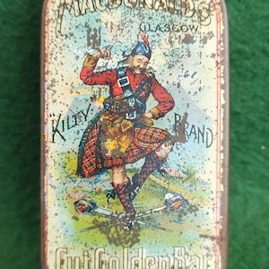 May include: Vintage rectangular tin with a Scottish theme. The tin features a colorful illustration of a man in a kilt, with the text "MacDonald's Glasgow" and "Kilty Brand". The tin also has the text "Cut Golden Bar" and "Established 1840".