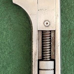 May include: Close-up of a vintage adjustable wrench with the name "SHELLEY" stamped on the top. The wrench is made of metal and has a screw mechanism for adjusting the jaw size. The background is a solid green color.