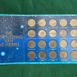 Peut inclure: Une pochette d'album bleue et noire avec le titre "DE VEROOVERING VAN DE HEMEL" et 20 petites pièces de monnaie dorées représentant différents avions. Les pièces sont disposées en grille et chaque pièce porte un nom et une date.