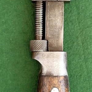 Puede incluir: Una llave inglesa ajustable vintage con mango de madera. La llave tiene un acabado plateado y un tornillo de ajuste roscado. El mango es de madera marrón con tres remaches de metal blanco.
