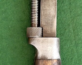 Puede incluir: Una llave inglesa ajustable vintage con mango de madera. La llave tiene un acabado plateado y un tornillo de ajuste roscado. El mango es de madera marrón con tres remaches de metal blanco.