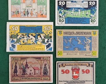 May include: A collection of vintage German paper tickets or coupons. The tickets are printed on thick paper with colorful illustrations and text. The tickets feature various scenes, including a mountain range, a building, and a group of people dancing. The tickets are in various denominations, including 10, 20, and 50.