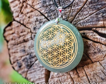 May include: A green stone pendant with a gold flower of life design. The pendant is on a black cord.