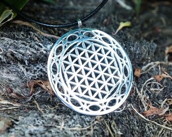 May include: A silver pendant necklace with a circular design featuring a flower of life pattern. The pendant is on a black leather cord.
