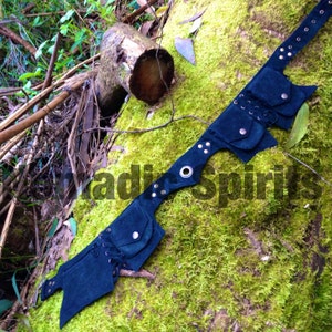 Peut inclure: Une ceinture en daim bleu foncé avec plusieurs poches et un œillet en métal. La ceinture est décorée de œillets argentés et présente un détail de laçage sur le devant.