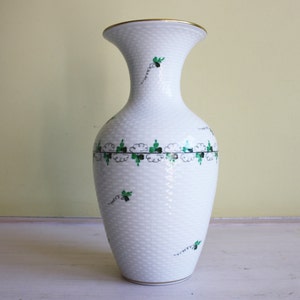 May include: White ceramic vase with a gold rim and green and black floral pattern.