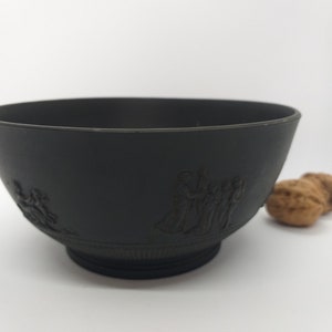 May include: A black ceramic bowl with a raised design of figures around the rim. The bowl is sitting on a white surface.