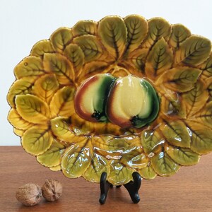 May include: A vintage ceramic serving dish with a raised design of green leaves and two pears. The dish is glazed in shades of green, brown, and yellow.