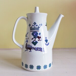 May include: White ceramic coffee pot with a blue and green floral design featuring a peacock and a crown.