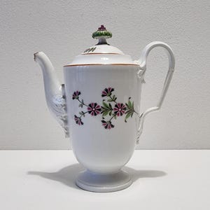 Peut inclure: Cafetière en porcelaine blanche avec un motif floral. La cafetière a un motif floral vert et rose avec un bouton vert et rose sur le couvercle.