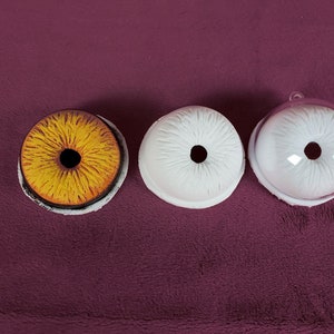 Puede incluir: Tres ojos redondos de pl&aacute;stico blanco con pupilas negras. Un ojo es amarillo con una pupila negra.