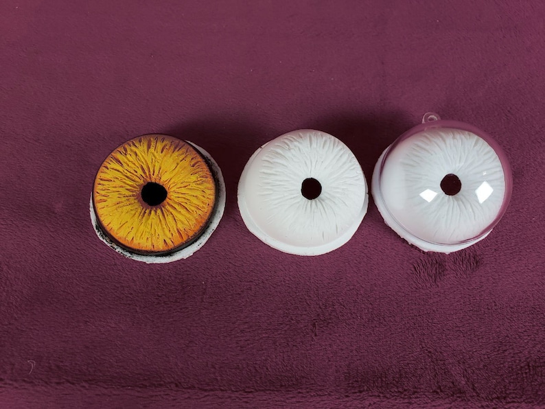 Puede incluir: Tres ojos redondos de pl&aacute;stico blanco con pupilas negras. Un ojo es amarillo con una pupila negra.