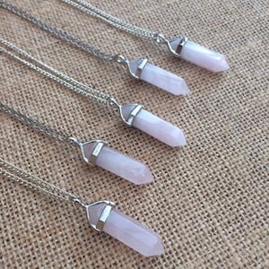 May include: Four silver necklaces with pink crystal point pendants. The necklaces are layered on a brown burlap background.