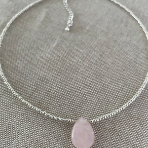 May include: A silver chain necklace with a light pink teardrop-shaped gemstone pendant.