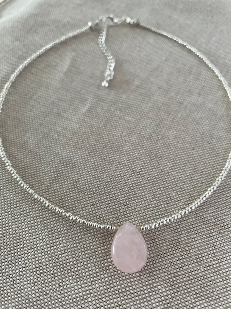 May include: A silver chain necklace with a light pink teardrop-shaped gemstone pendant.