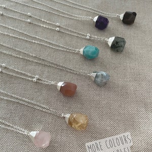 May include: A collection of gemstone necklaces with silver chains. The gemstones are various colors, including purple, blue, brown, yellow, and pink. The text "MORE COLOURS AVAILABLE!" is visible in the bottom right corner.