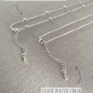 Op de afbeelding: Close-up van twee verzilverde kettingen. E&eacute;n is een satellietketting met kleine, gelijkmatig verdeelde kralen. De andere is een verzilverde ketting. Beide hebben verstelbare sluitingen. Tekst is zichtbaar.
