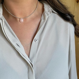 May include: A silver chain necklace with a light pink teardrop-shaped pendant.