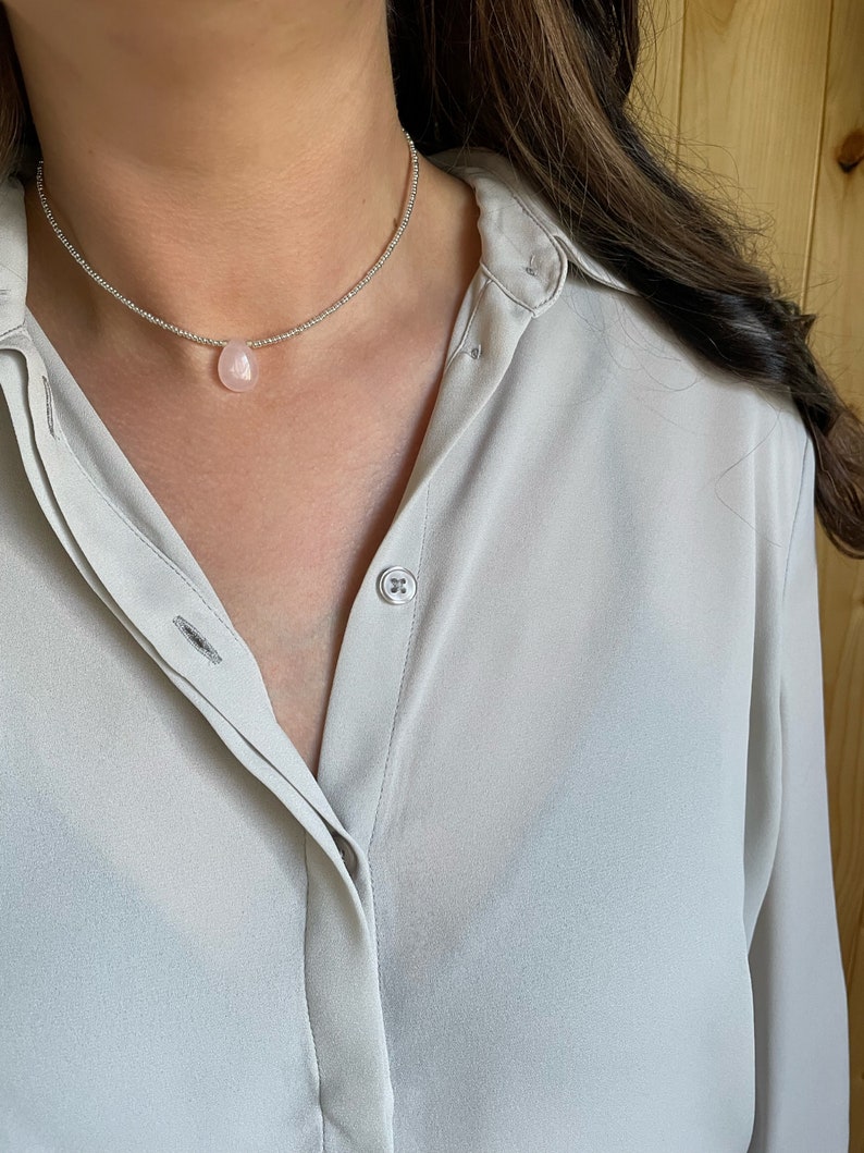 May include: A silver chain necklace with a light pink teardrop-shaped pendant.