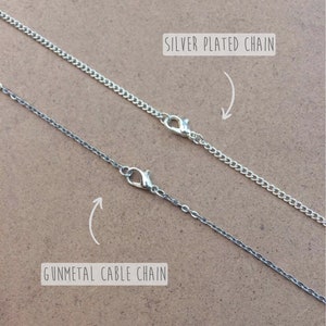 May include: Two silver chains, one silver plated chain and one gunmetal cable chain, are shown on a brown surface. The chains are both closed with a lobster clasp.