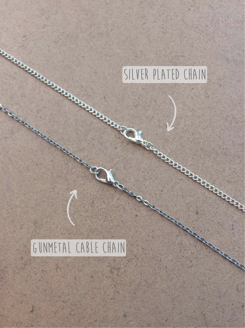 May include: Two silver chains, one silver plated chain and one gunmetal cable chain, are shown on a brown surface. The chains are both closed with a lobster clasp.